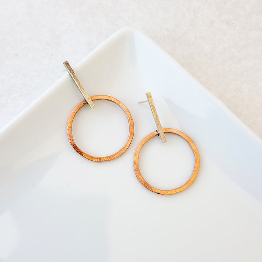 Hand-fabricated post earrings of copper circles hanging from sterling silver bar, both with a bolder gauge, square form.