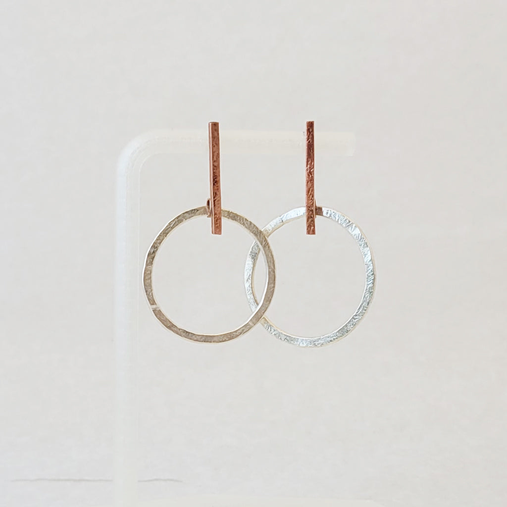 Hand-fabricated post earrings of sterling silver circles hanging from copper bar, both with a bolder gauge, square form.