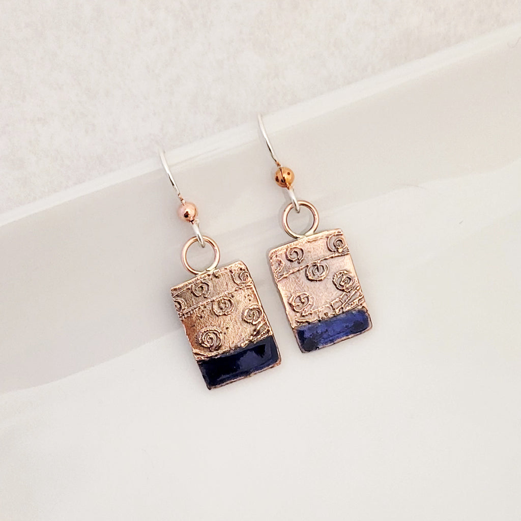 Handmade earrings.  Hand-fabricated copper rectangle, etched with swirl design, bottom with cobalt blue enamel work