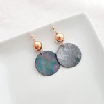 Handmade earrings of copper circles with iridescent charcoal patina suspended from copper bead.
