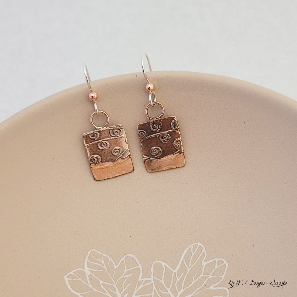 Handmade earrings.  Hand-fabricated copper rectangle, etched with swirl design, bottom with blush enamel work