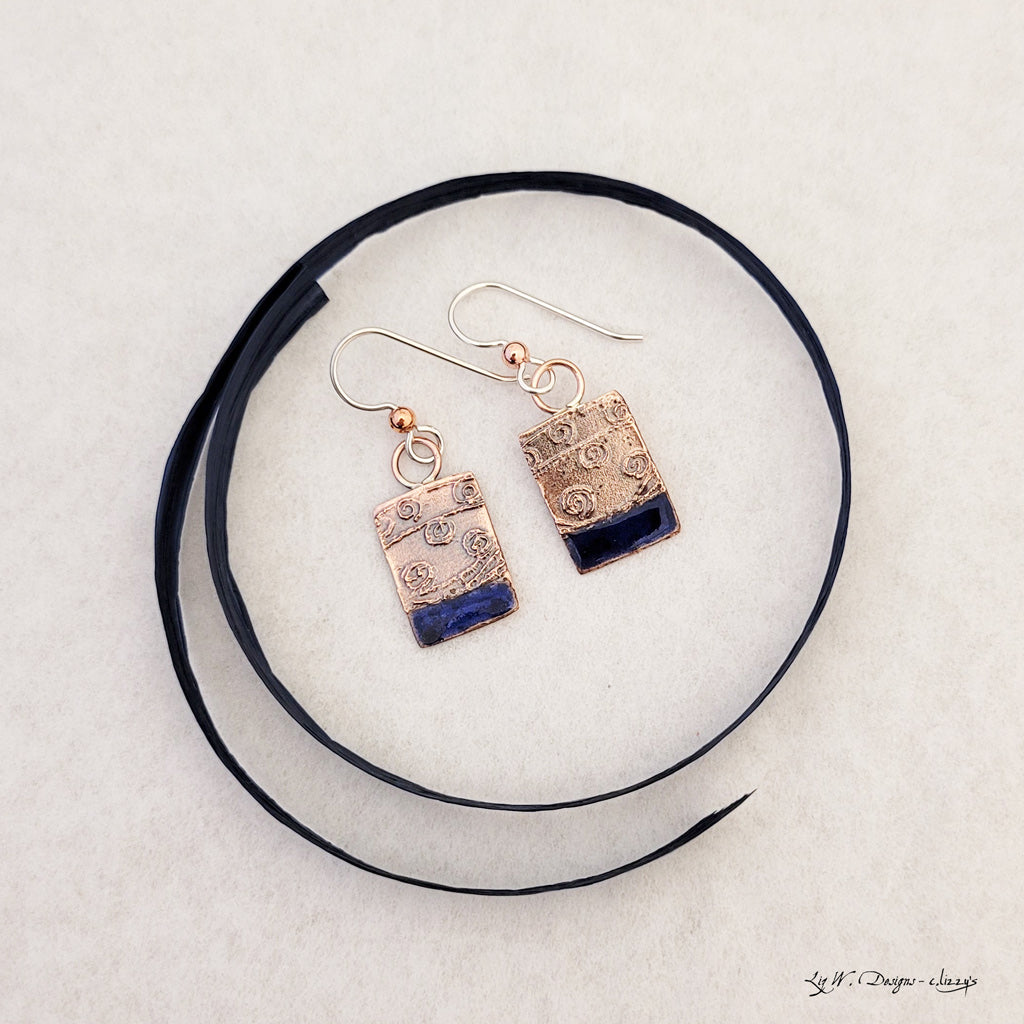 Handmade earrings. Hand-fabricated copper rectangle, etched with swirl design, bottom with cobalt blue enamel work