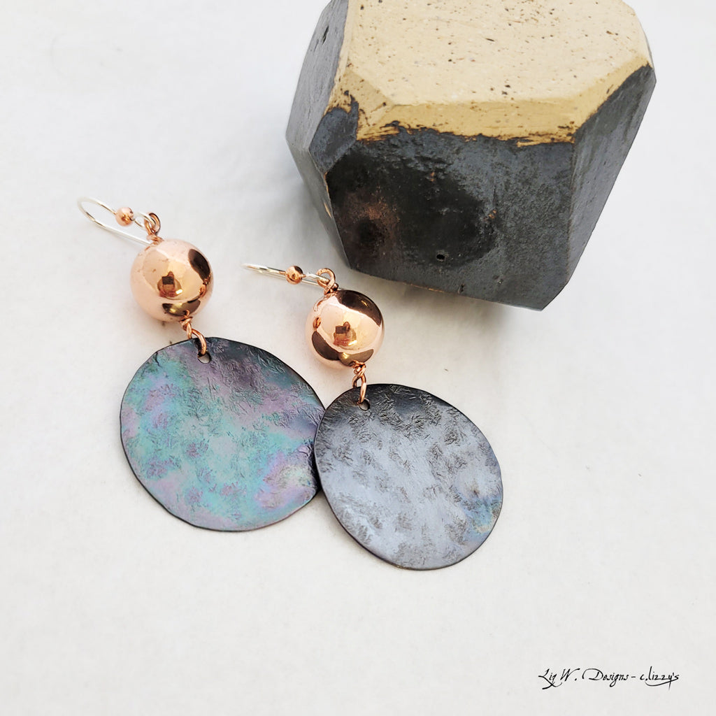 Handmade earrings of copper circles with iridescent charcoal patina suspended from copper bead.