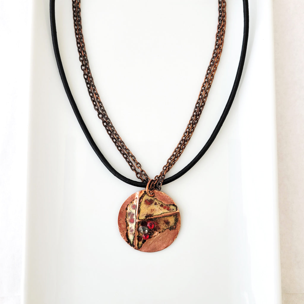 Necklace with red and neutral enamel on textured copper circle with copper chain and black leather together.