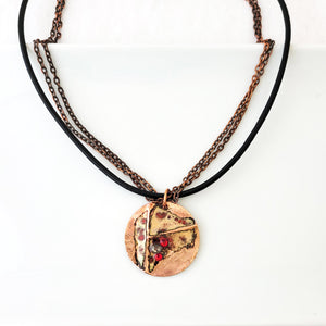Necklace with red and neutral enamel on textured copper circle with copper chain and black leather together.