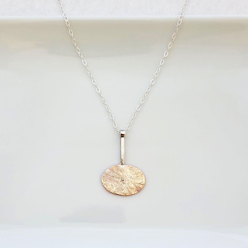 Handmade necklace of sterling silver layers over copper oval shape from sterling bar.