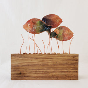 Hand-fabricated copper sunny fish in varied enamel tones of greens, blues and blush with copper lake grass on wood base.