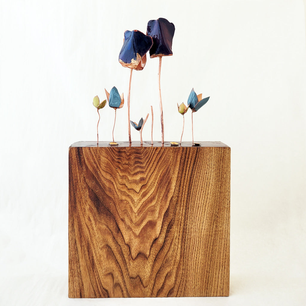 Hand-fabricated copper tulips and flowers enameled in blue, powder blue, lime green and yellow/goldenrod on copper stems on found wood base.