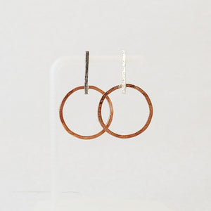Hand-fabricated post earrings of copper circles hanging from sterling silver bar, both with a bolder gauge, square form.