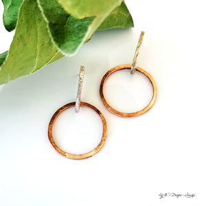 Hand-fabricated post earrings of copper circles hanging from sterling silver bar, both with a bolder gauge, square form.