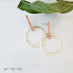 Hand-fabricated post earrings of sterling silver circles hanging from copper bar, both with a bolder gauge, square form.