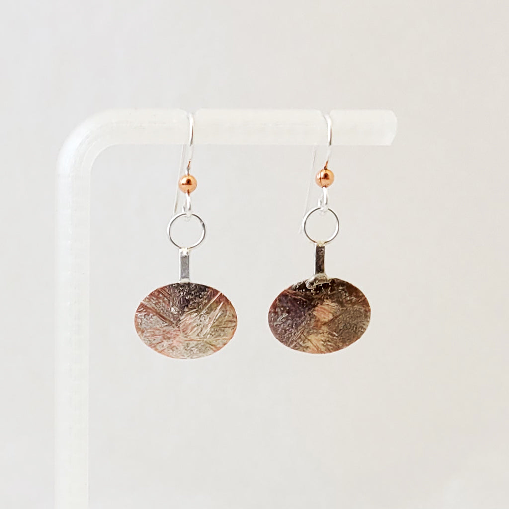 Handmade earrings of sterling silver layers over copper on side oval shape from sterling bar.