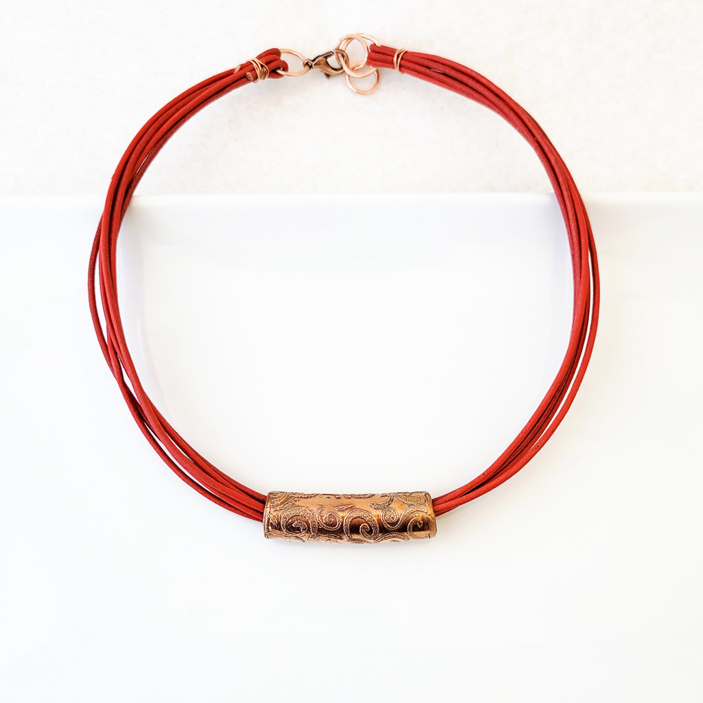 Etched swirl design on copper tube on poppy red leather necklace.