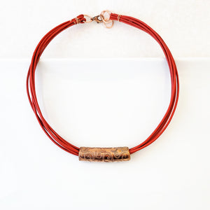 Etched swirl design on copper tube on poppy red leather necklace.