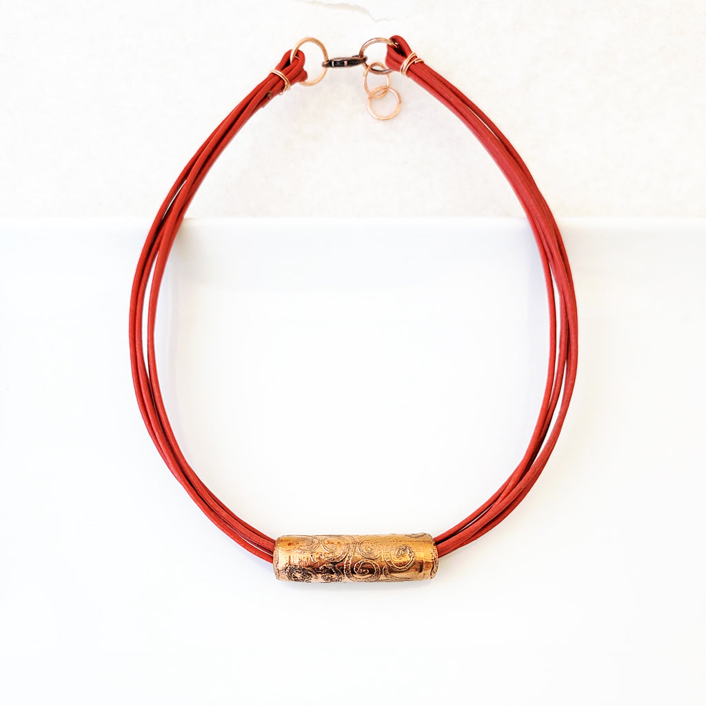 Etched swirl design on copper tube on poppy red leather necklace.
